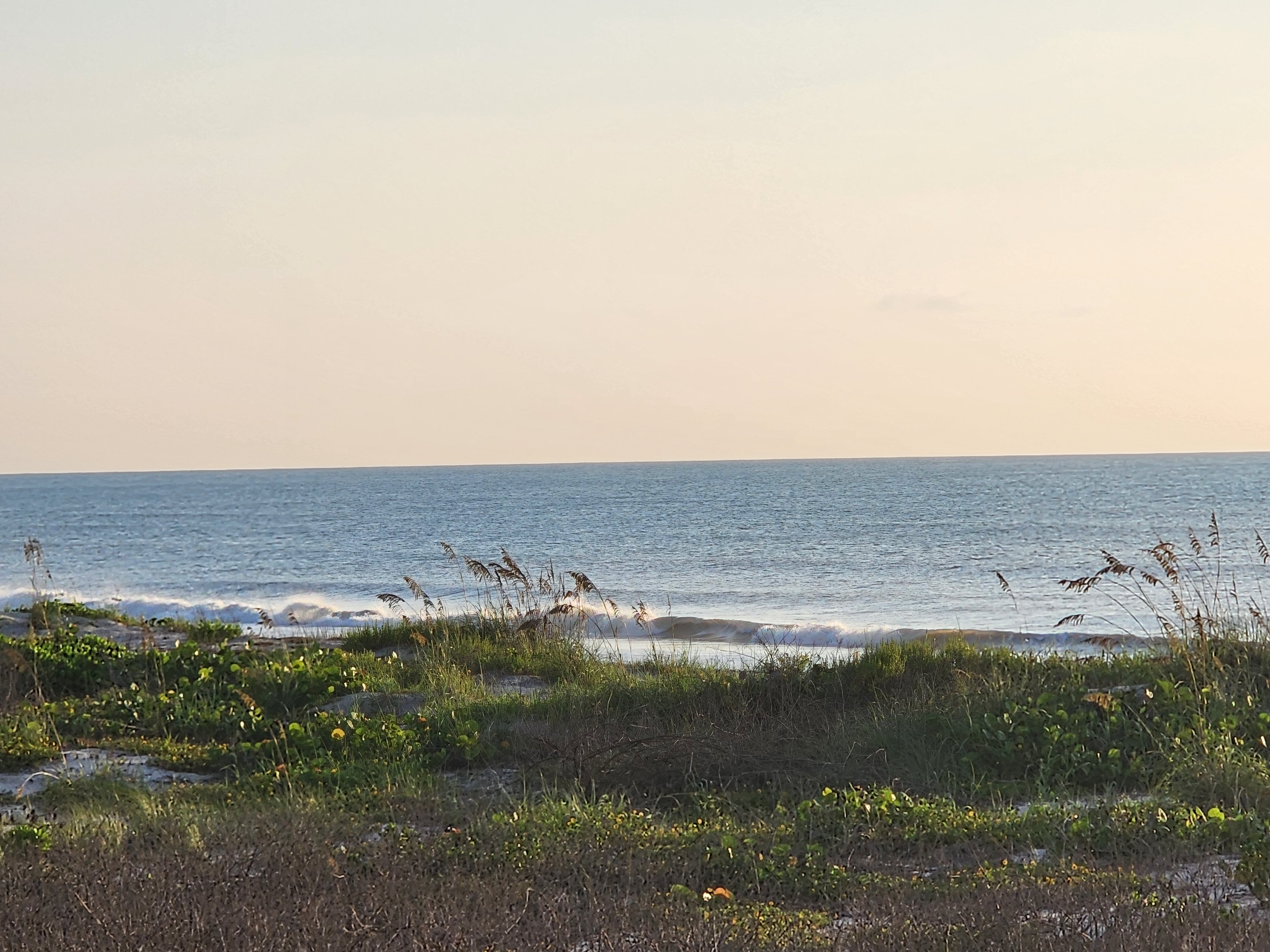 Hazy sunrise over gentle surf and sea oats, South Cocoa Beach