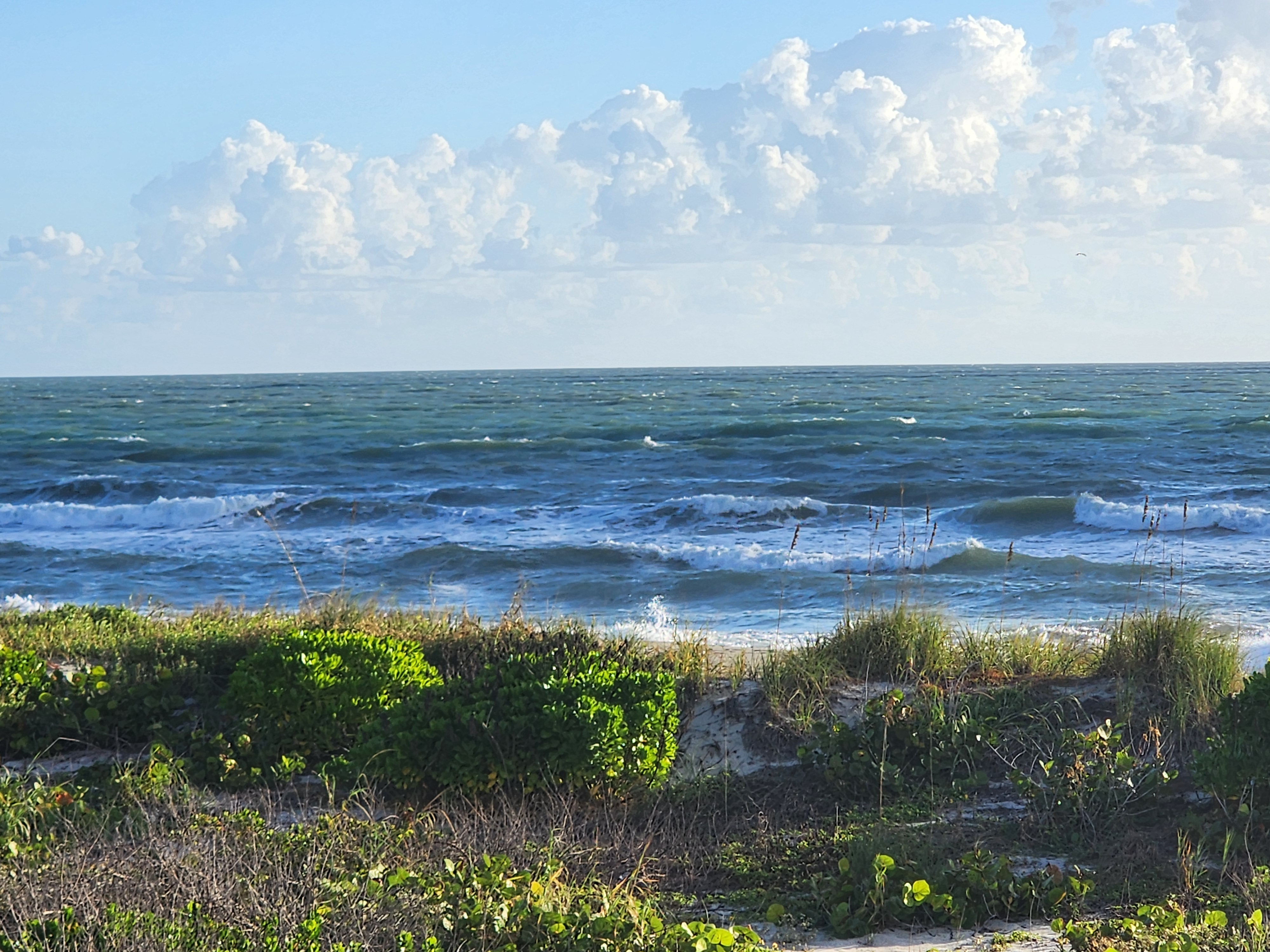 Choppy, whitecapped ocean with broken waves across the inside bar beneath towering cumulus clouds